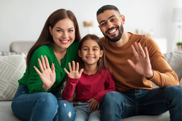 Family sitting on a couch waving